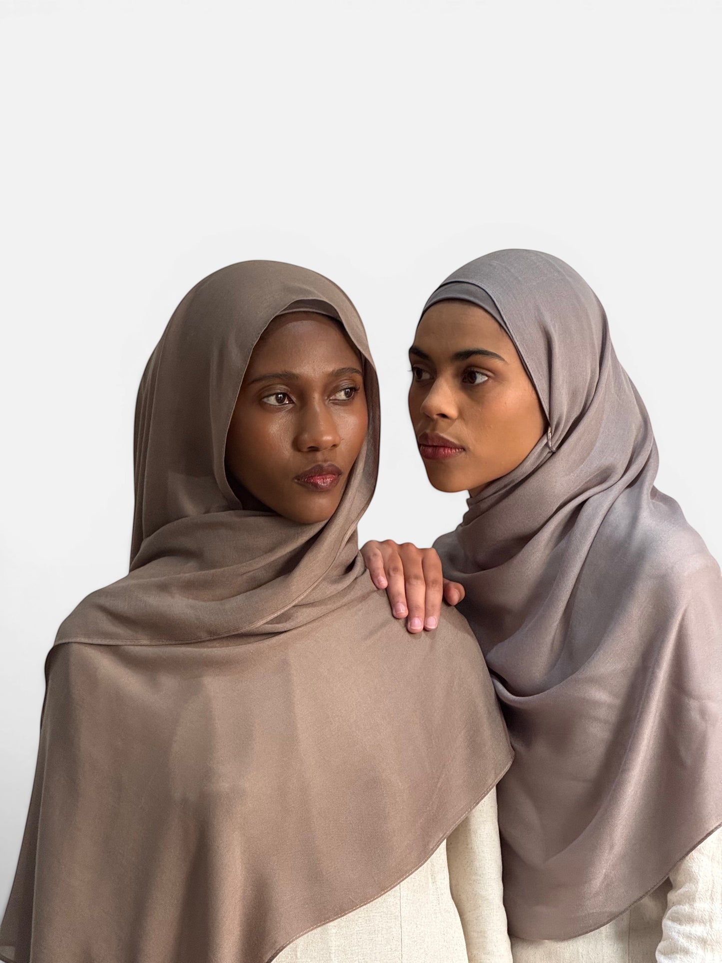Two models wearing SAHR STUDIOS pebble-toned modal hijabs with matching undercaps, showcasing a soft, breathable drape.